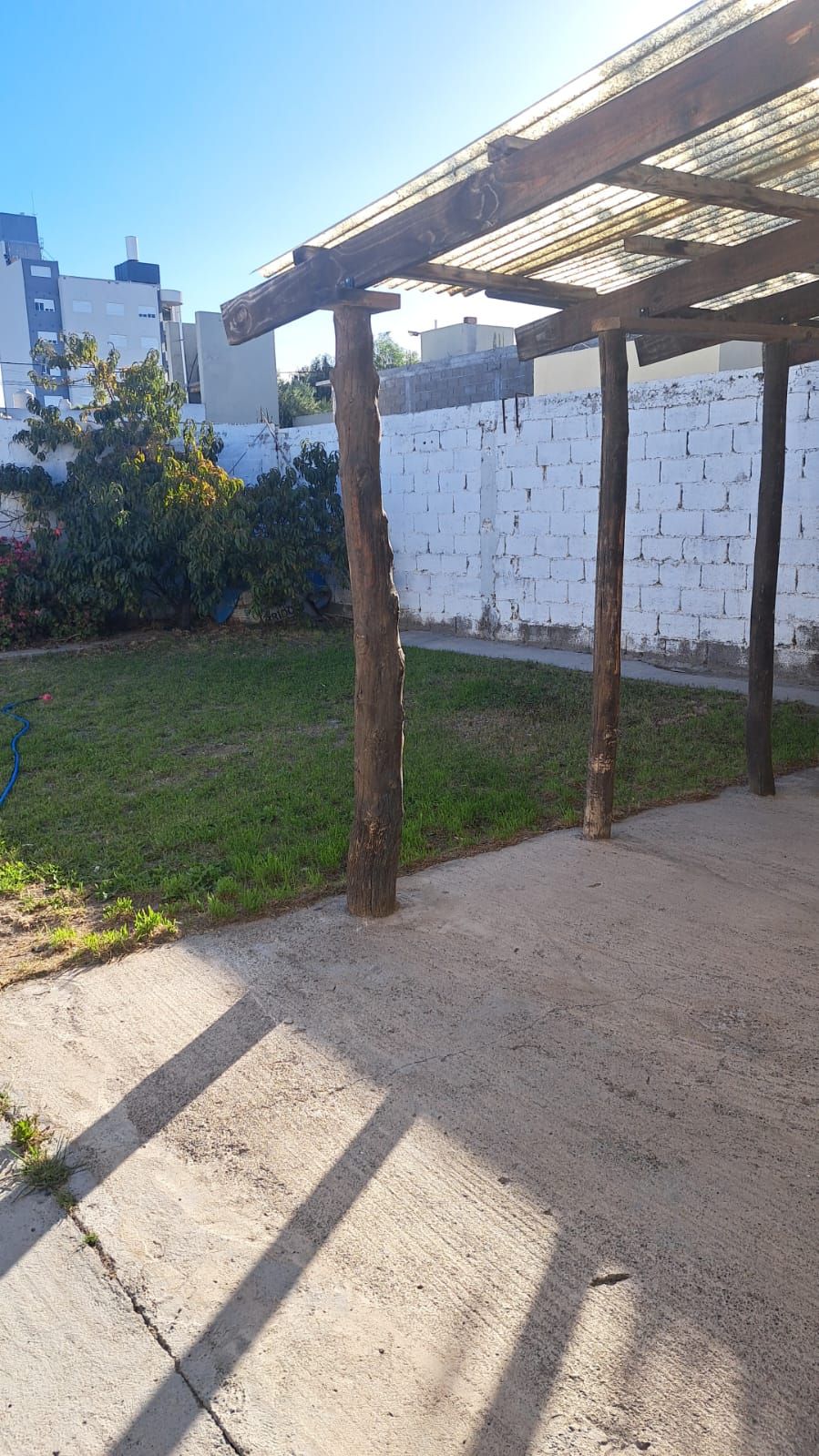 Patio con césped y pérgola de madera, con el cielo despejado.