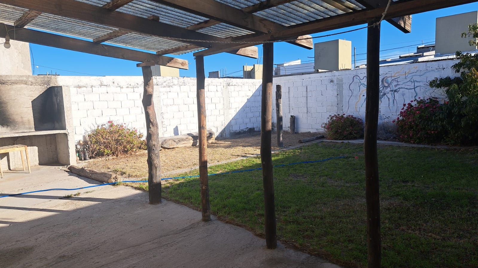 Galería techada con pérgola de madera frente al patio con césped.